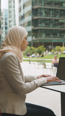 Vertikales-Video-Einer-Muslimischen-Geschäftsfrau,-Die-Draußen-In-Stadtgärten-Sitzt-Und-Am-Laptop-Arbeitet-1